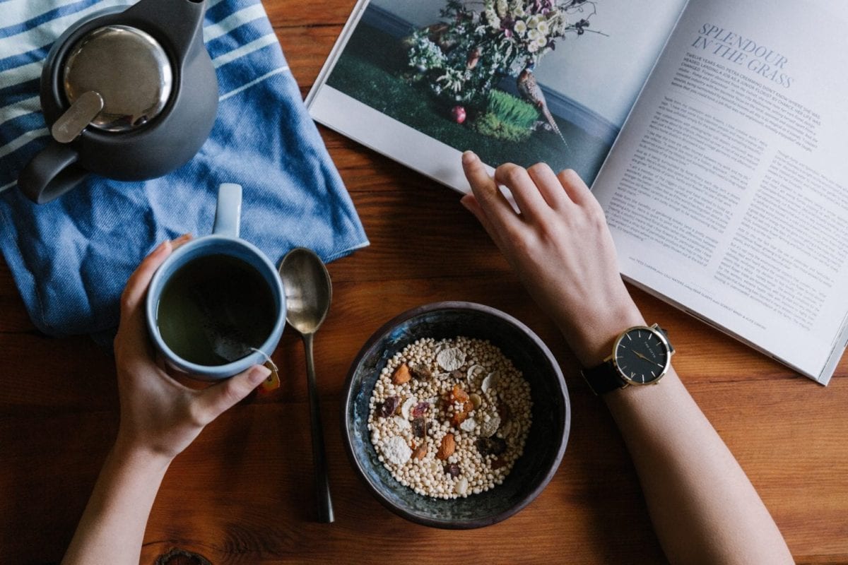 Photo of person reading a magazine with a cup of tea and bowl of cereal