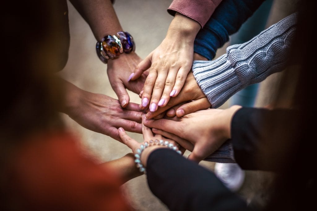 Photograph of many peoples hands all touching in centre point to form a team bond