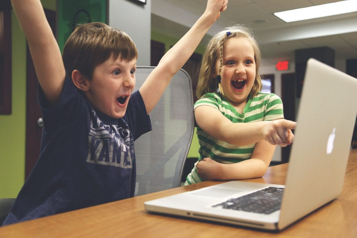 Two children looking shocked and pleased at something on a laptop screen