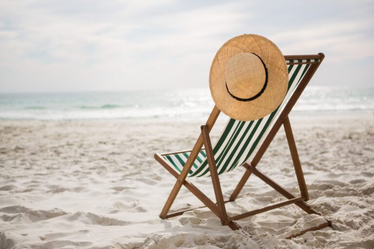 Photo of a straw hat hanging on the back of a deckchair on a beach with the sea in the background